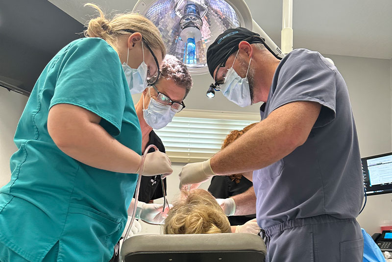 Doctor performing dental procedure surgery with patient inside of dental partice